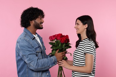 Photo of International dating. Happy couple with bouquet of roses on pink background