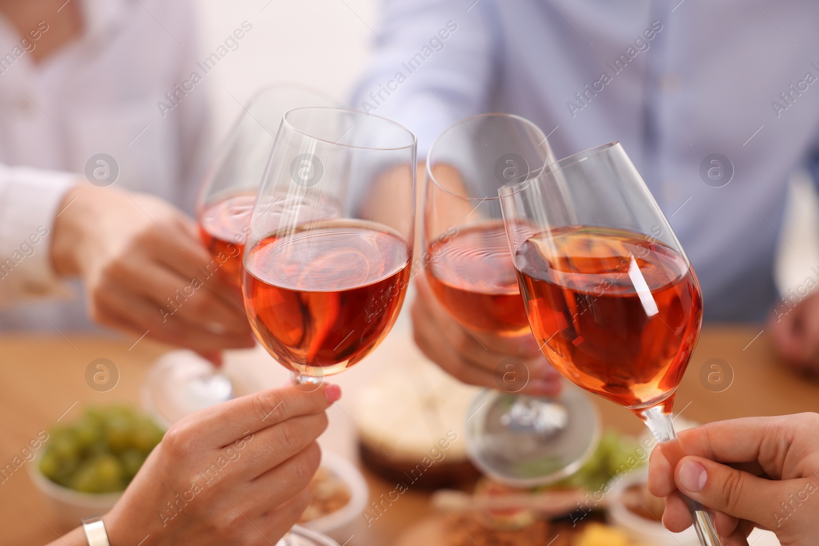 Photo of People clinking glasses with rose wine above wooden table indoors, closeup