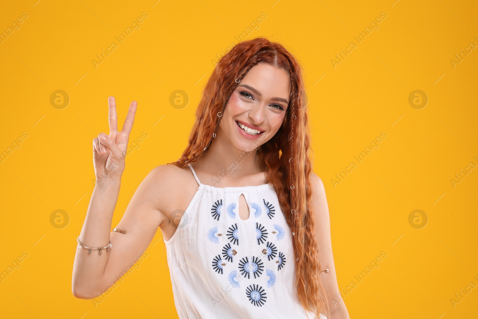 Photo of Beautiful young hippie woman showing V-sign on orange background