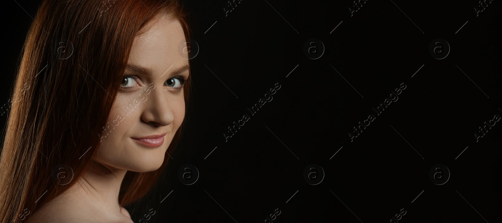 Photo of Candid portrait of happy young woman with charming smile and gorgeous red hair on dark background, space for text