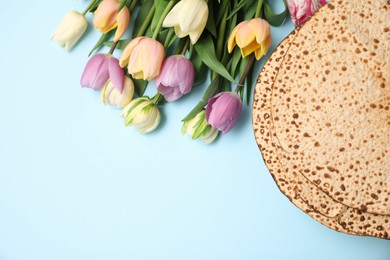Photo of Tasty matzos and fresh tulips on light blue background, flat lay with space for text. Passover (Pesach) celebration