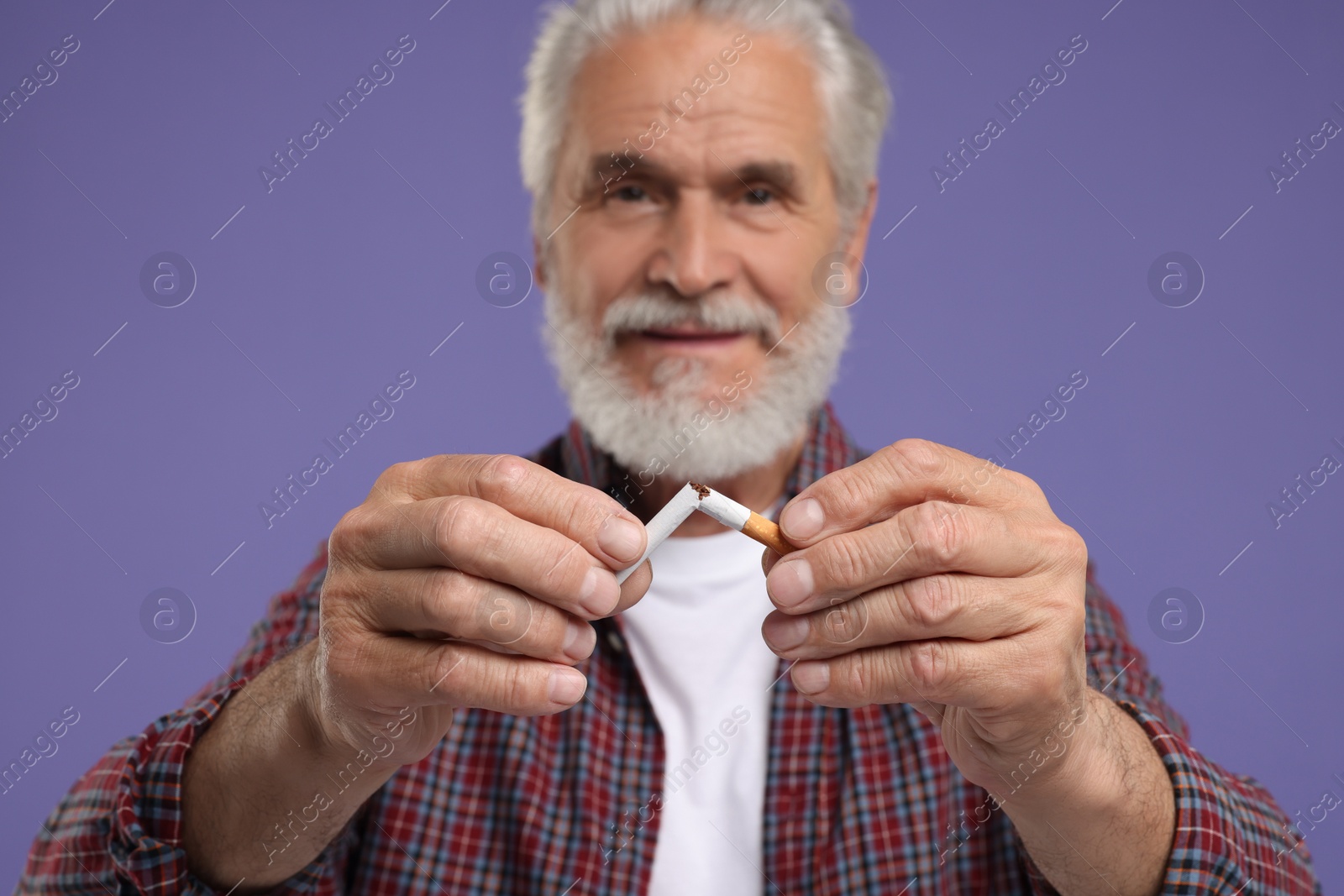 Photo of Stop smoking concept. Senior man breaking cigarette on purple background, selective focus