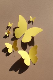 Photo of Yellow paper butterflies on light brown background, top view