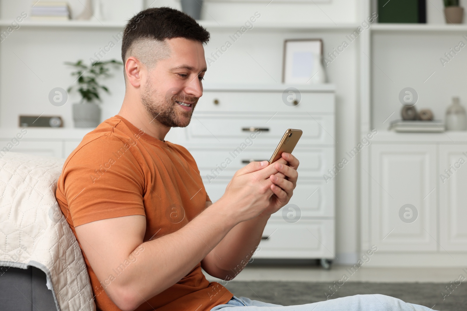 Photo of Handsome man sending message via smartphone at home. Space for text