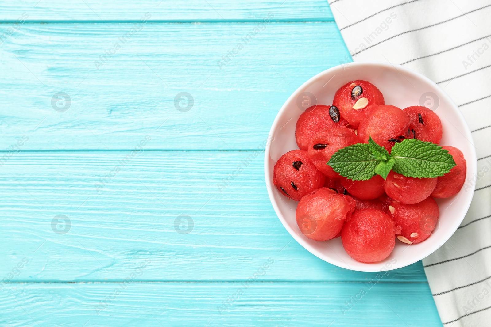 Photo of Bowl of watermelon balls with mint on light blue wooden table, flat lay. Space for text