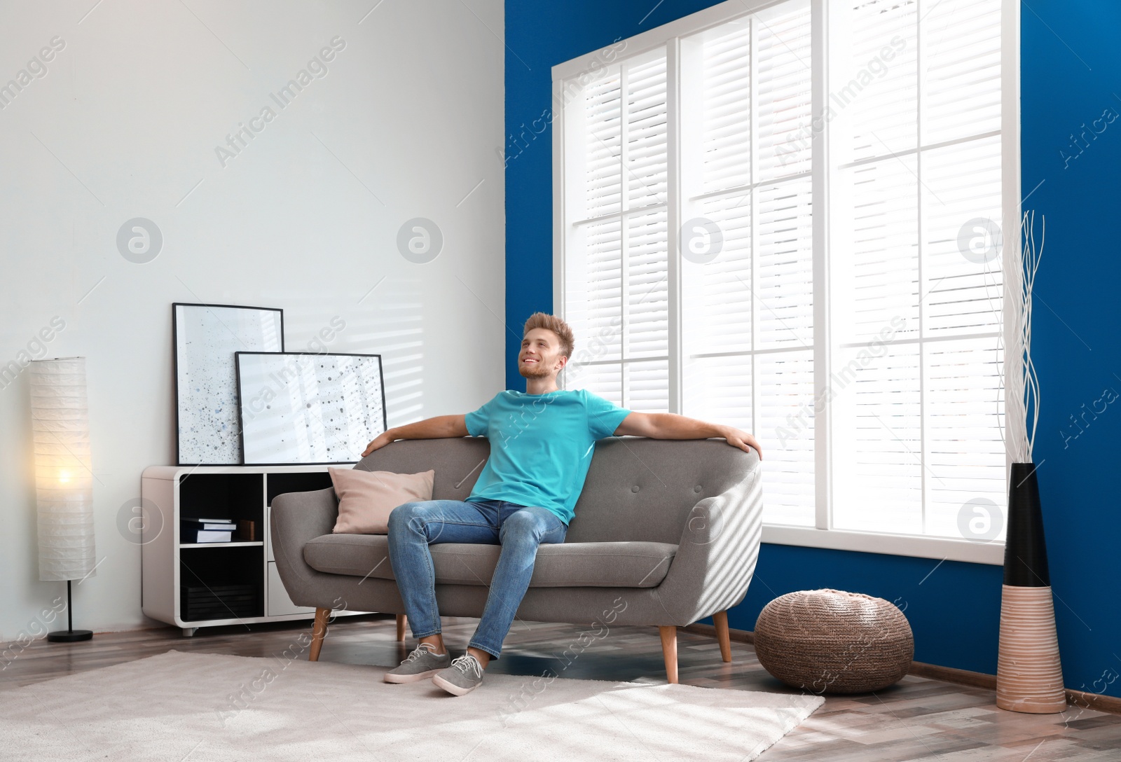 Photo of Happy young man resting on sofa under air conditioner at home