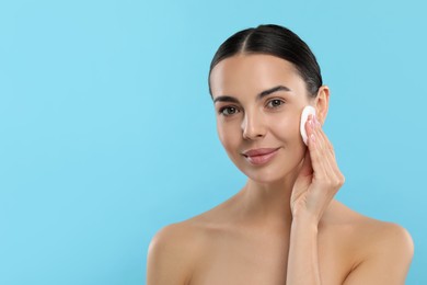 Photo of Beautiful woman removing makeup with cotton pad on light blue background, space for text