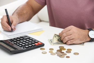 Photo of Young man counting money at white table indoors, closeup