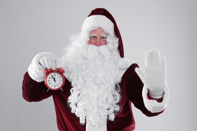 Photo of Santa Claus holding alarm clock on light grey background. Christmas countdown