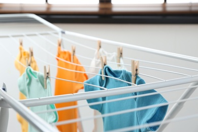 Photo of Different cute baby onesies hanging on clothes line indoors. Laundry day