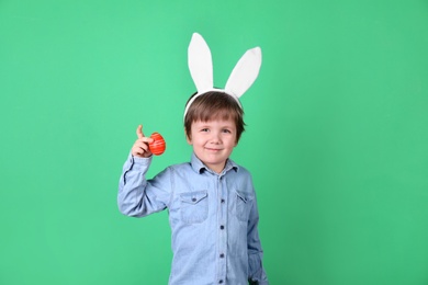 Photo of Cute little boy wearing bunny ears with dyed Easter egg on green background