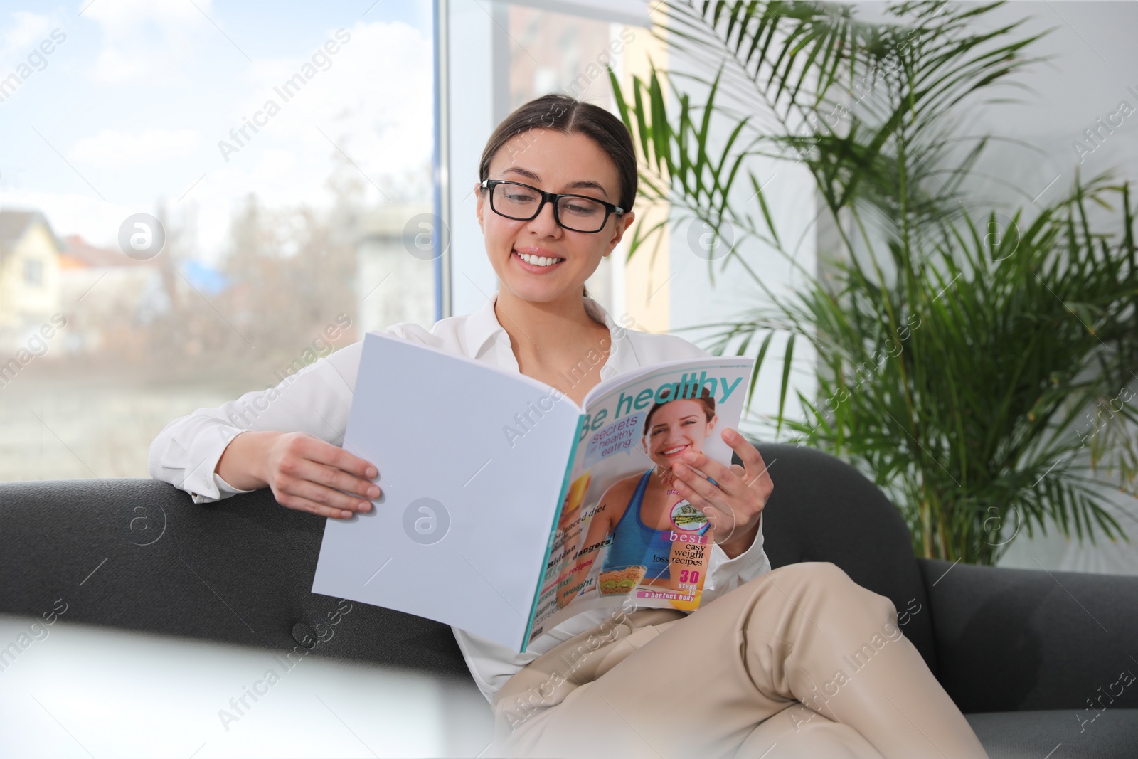 Photo of Happy woman reading magazine on sofa in office