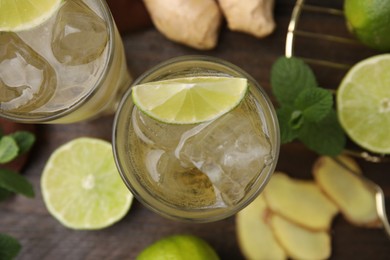 Photo of Glasses of tasty ginger ale with ice cubes and ingredients on wooden table, top view