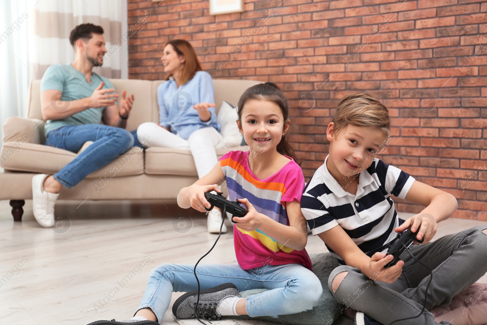 Photo of Cute children playing video games while parents resting on sofa at home