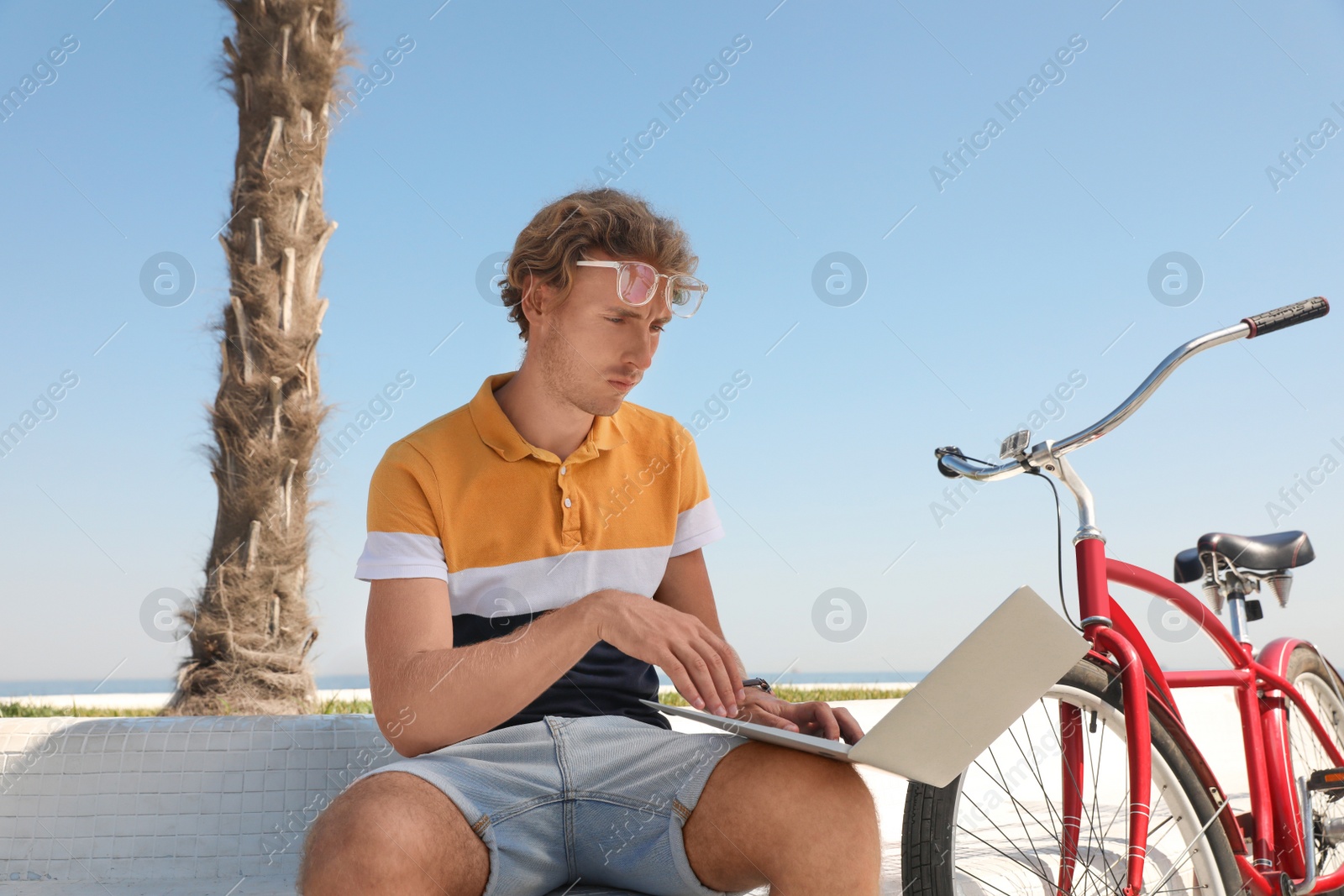Photo of Attractive man with laptop and bike outdoors on sunny day