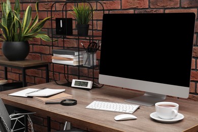 Photo of Cosy workspace with computer on desk and potted plants near brick wall at home