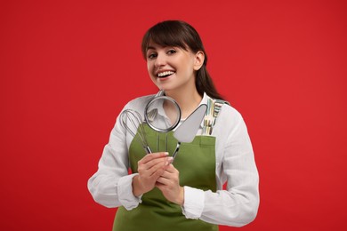Photo of Happy confectioner in apron holding professional tools on red background