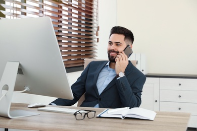 Handsome businessman talking on phone while working with computer at table in office