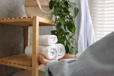 Photo of Woman putting rolled towels onto shelf indoors, closeup