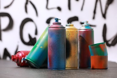 Many spray paint cans and caps on gray surface against white wall with different drawn symbols