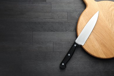 Photo of One sharp knife and board on black wooden table, top view. Space for text