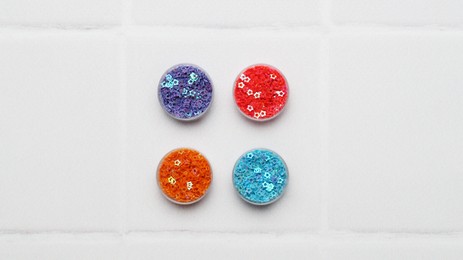 Photo of Many different colorful sequins in containers on white tiled background, top view