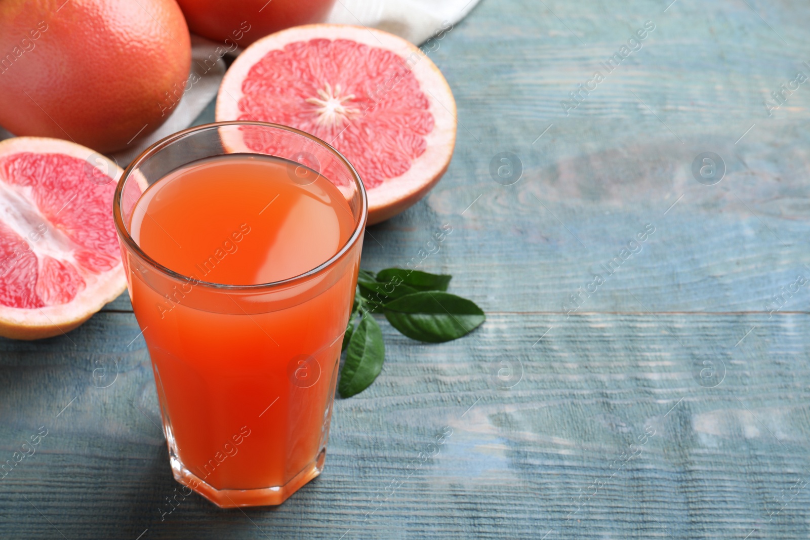 Photo of Tasty freshly made grapefruit juice on blue wooden table. Space for text