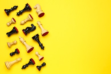 Photo of Many different chess pieces on yellow background, flat lay. Space for text