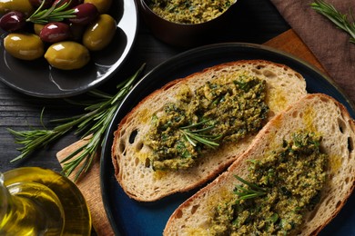 Photo of Tasty bruschettas with pesto and rosemary on black wooden table, flat lay