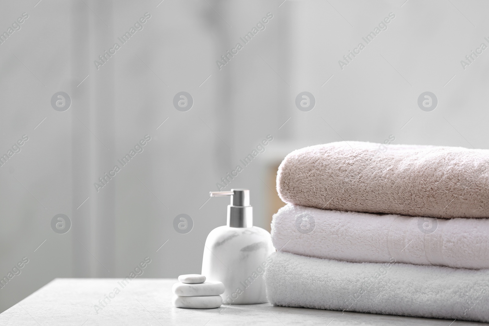 Photo of Clean towels, spa stones and soap dispenser on table in bathroom. Space for text