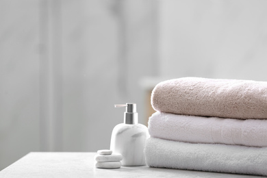 Photo of Clean towels, spa stones and soap dispenser on table in bathroom. Space for text