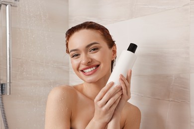 Happy young woman with bottle of shampoo in shower