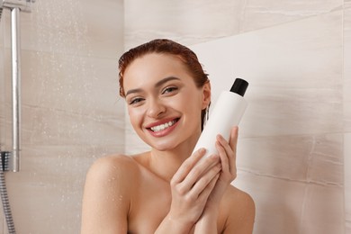 Photo of Happy young woman with bottle of shampoo in shower