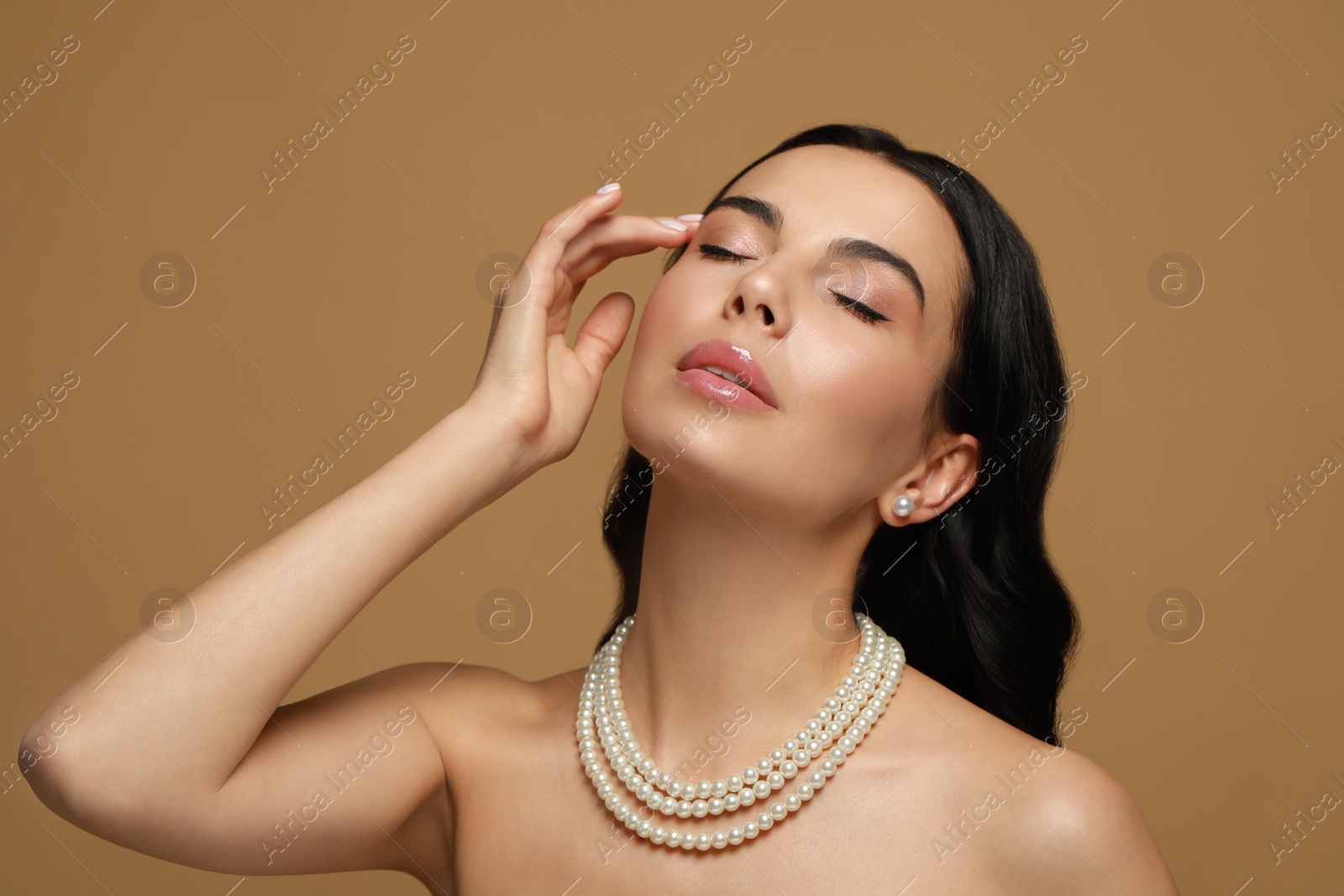 Photo of Young woman wearing elegant pearl jewelry on brown background