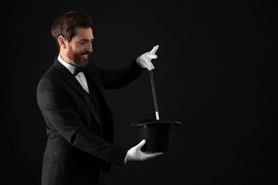 Photo of Happy magician showing magic trick with top hat on black background, space for text