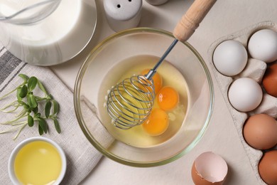 Flat lay composition with raw eggs and whisk in bowl on light table
