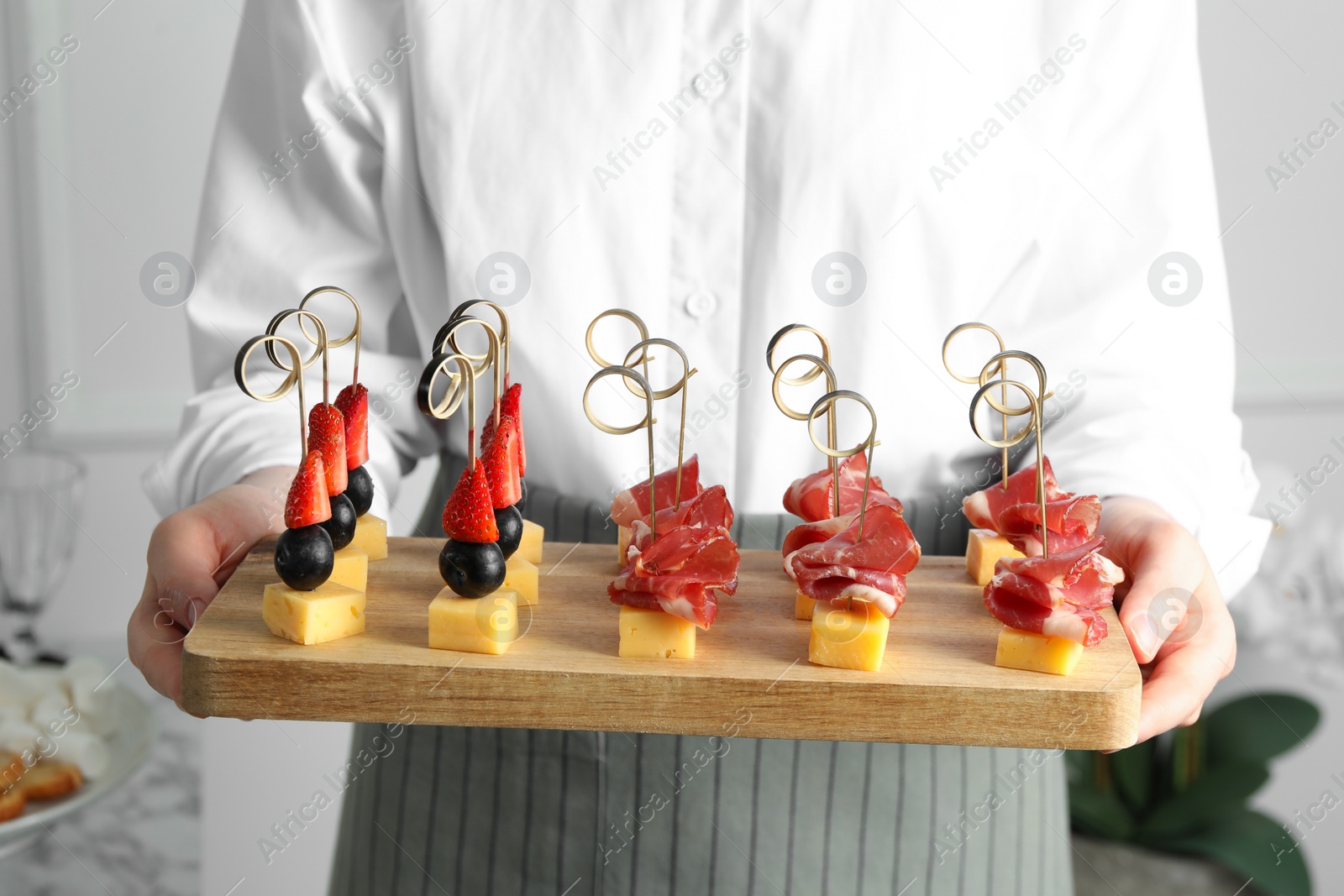 Photo of Woman holding tray of different tasty canapes indoors, closeup