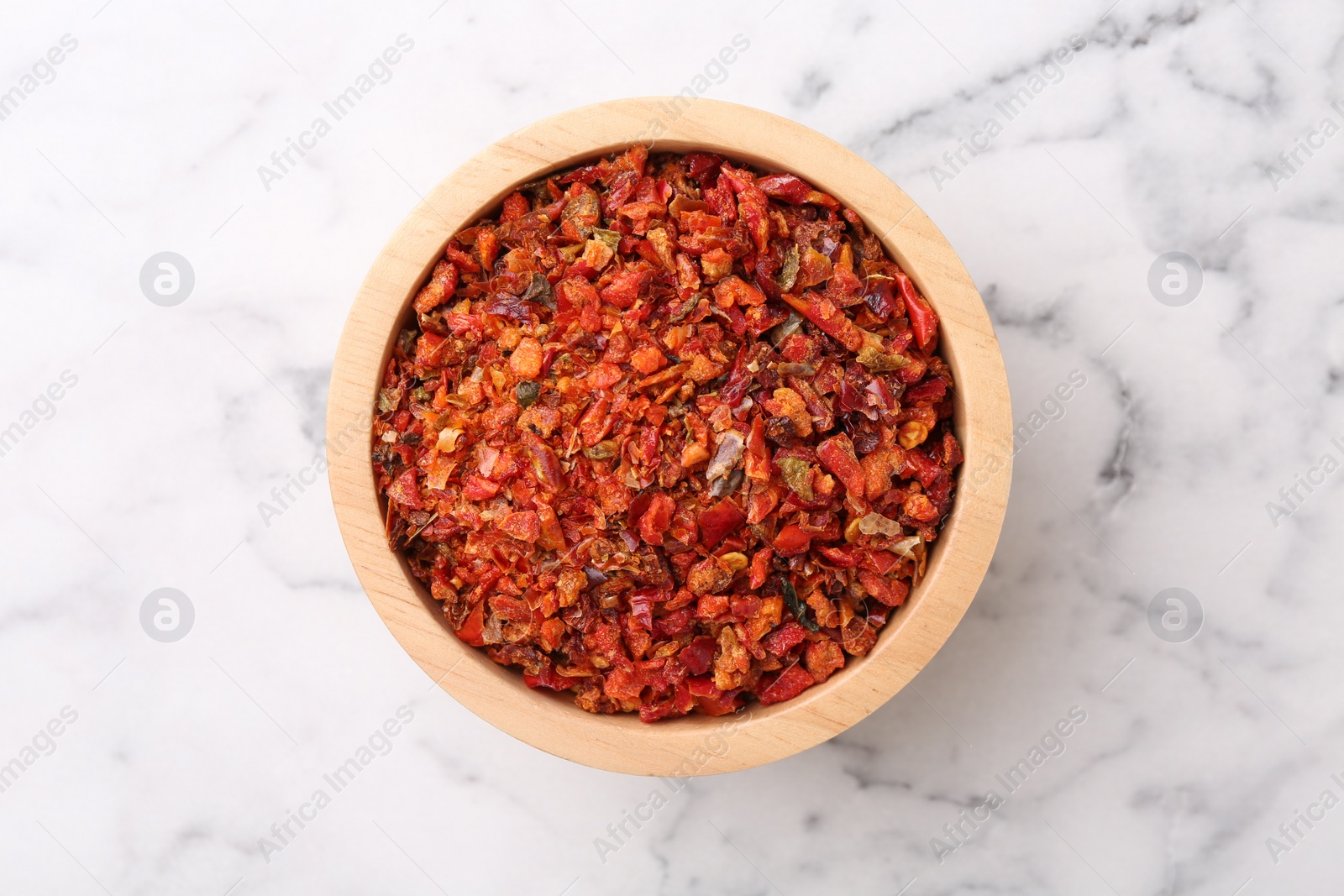 Photo of Chili pepper flakes in bowl on white marble table, top view