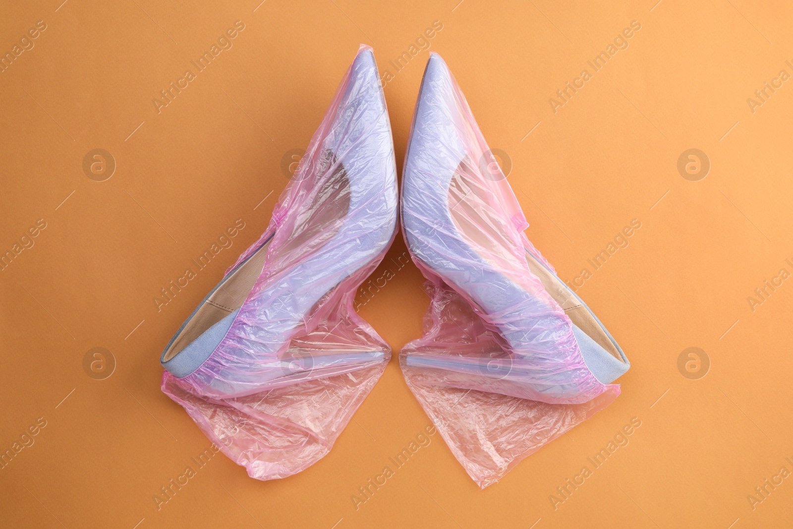 Photo of High heels in shoe covers on brown background, top view