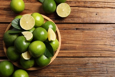 Photo of Fresh limes and green leaves on wooden table, top view. Space for text