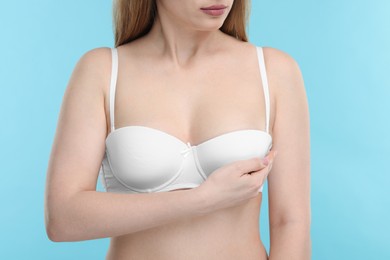Photo of Mammology. Young woman doing breast self-examination on light blue background, closeup