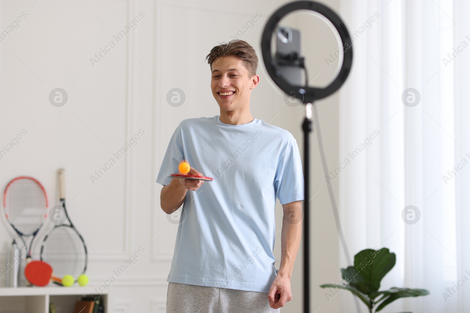 Photo of Smiling sports blogger with table tennis racket and ball streaming online fitness lesson at home