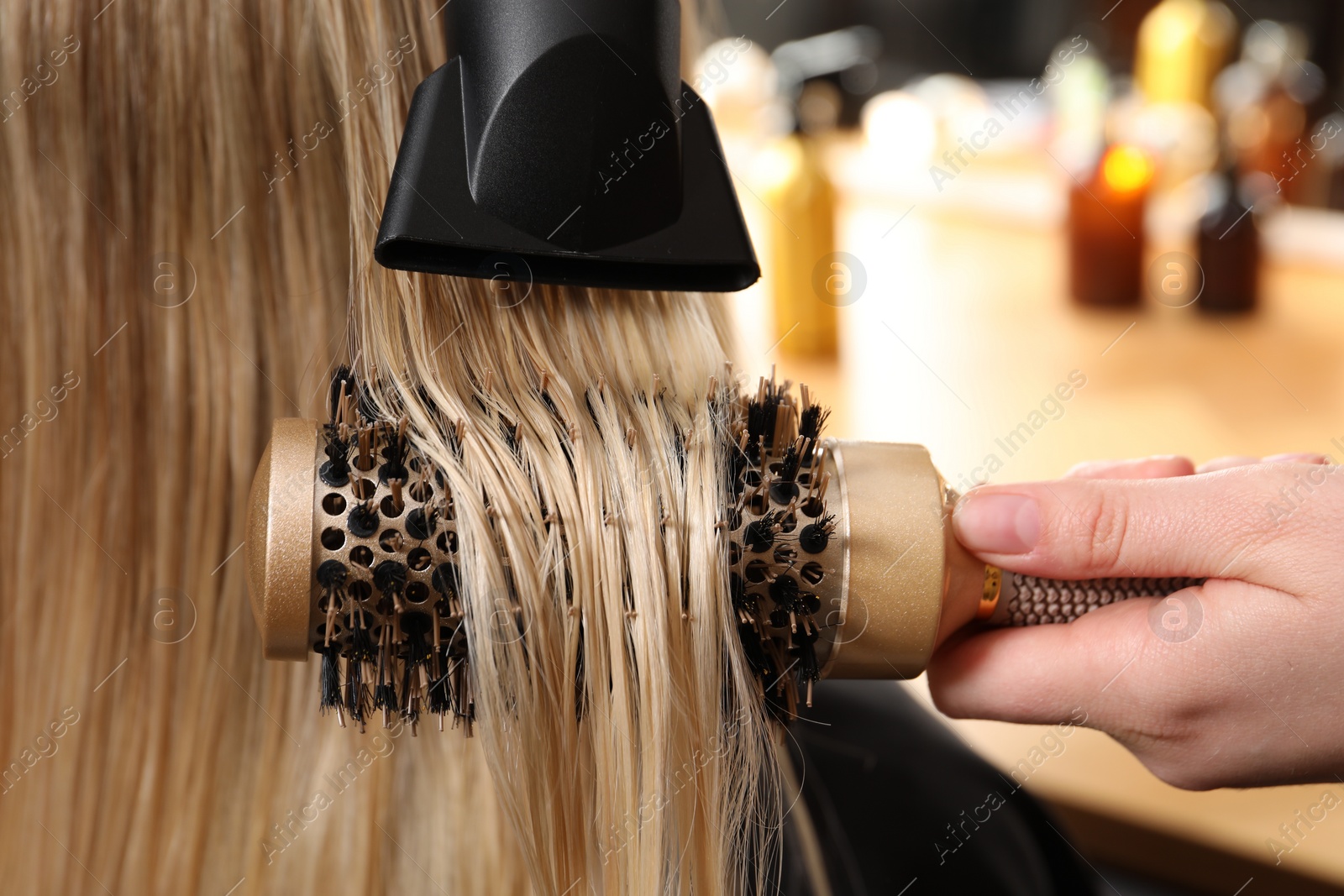 Photo of Hairdresser blow drying client's hair in salon, closeup