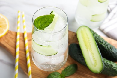 Photo of Tasty fresh cucumber water, sliced lemon and basil on white table, closeup