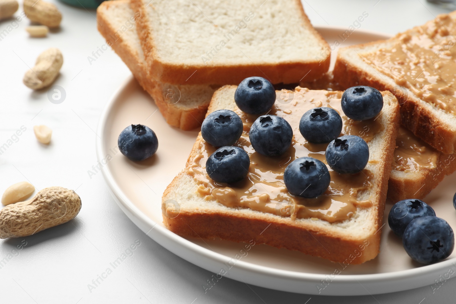 Photo of Delicious toasts with peanut butter and blueberries on white table, closeup