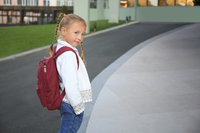 Photo of Cute little girl with backpack on city street. Space for text