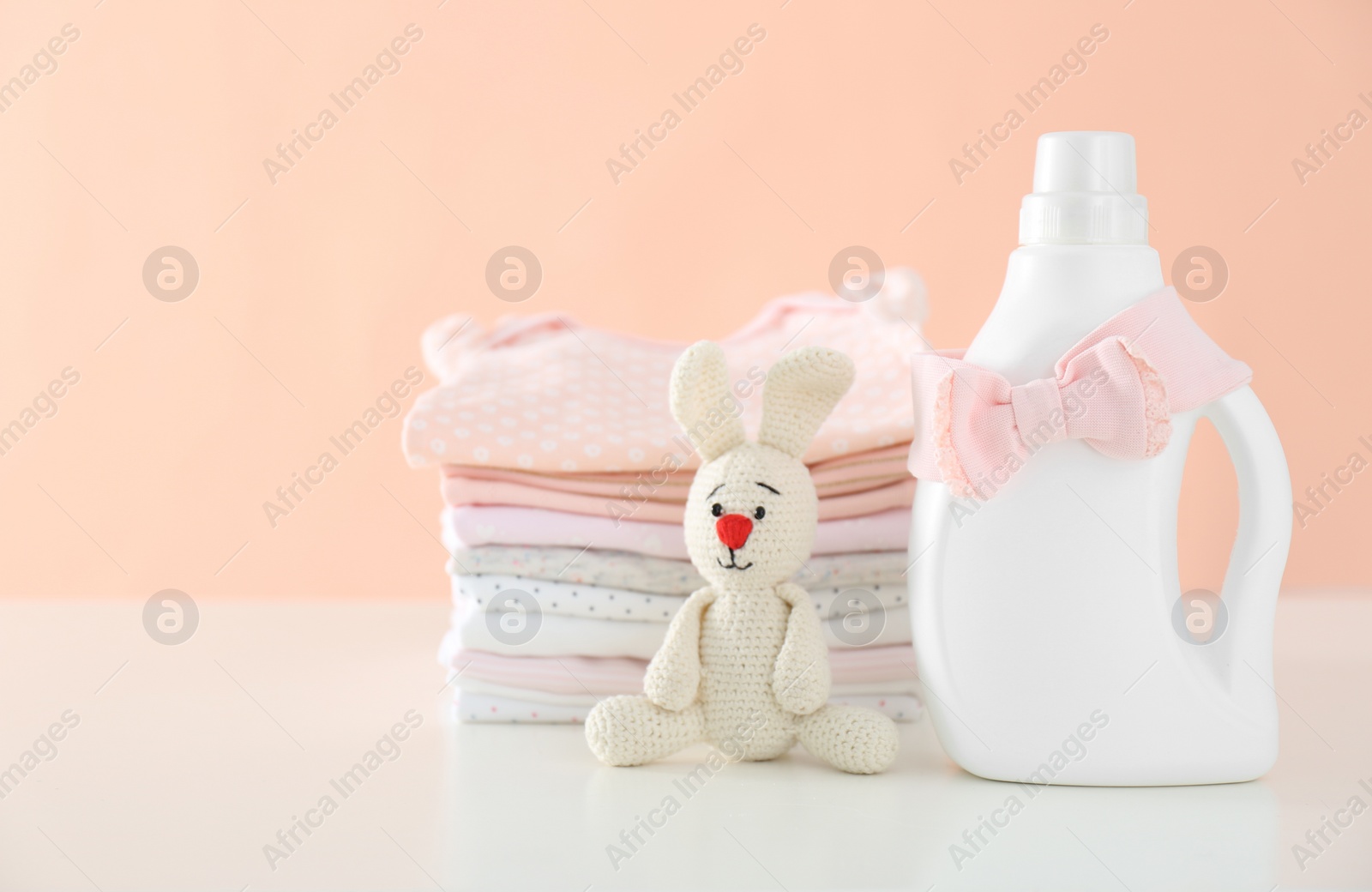 Photo of Detergent, toy and children's clothes on white table near pink wall