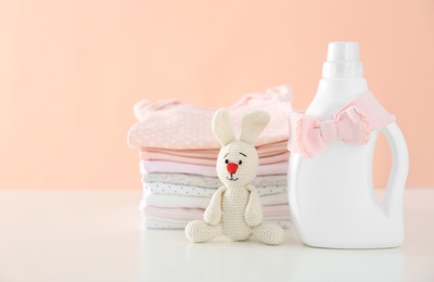 Photo of Detergent, toy and children's clothes on white table near pink wall