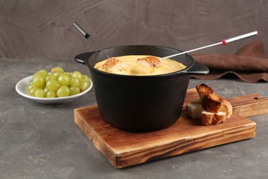 Photo of Fondue pot with tasty melted cheese, forks, bread and grapes on grey table