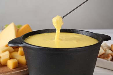 Photo of Dipping piece of ham into fondue pot with tasty melted cheese at table, closeup
